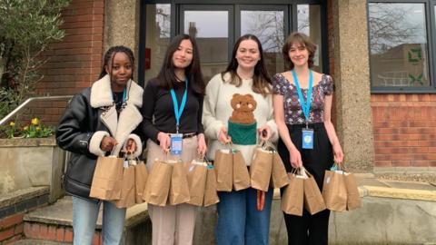 Four female students standing outside St Martins Housing Trust holding hygiene kits