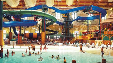 A large warehouse-like indoor space with covered slides towering over a shallow pool