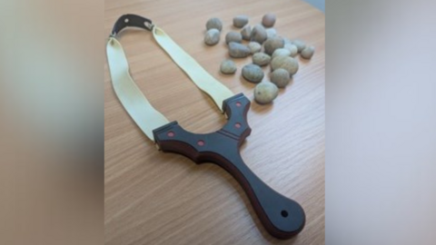 An image of a catapult sent over by Kent Police. The catapult has a black handle and white elastic. A number of stones are pictured to the right of the catapult.