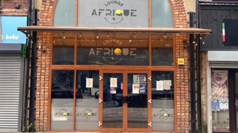 Front of the club. It has large windows with wooden frames and the name Lounge Afrique in large letters. 