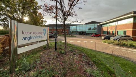 The Anglian Water headquarters in Huntingdon. There is a sign reading 'Love every drop – Anglian Water' in the foreground and an office building in the background