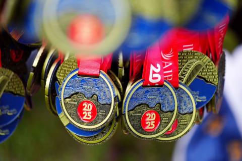 A collection of 2025 Great North Run medals. The medals are round with the medal divided into two sections, one coloured blue and one black with the outline of a map engraved on them and a round section coloured red with 2025 in them. The medals are on red ribbons