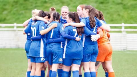 Thornaby Women are in a circular huddle in blue kits, the keeper is wearing orange. 