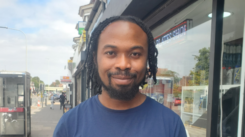 Man with short dreadlocks on a street in blue t shirt