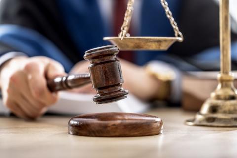 A close up shot of a wooden mallet held over a wood base, in a tribunal setting.