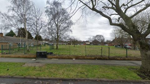 The land off Showell Circus in Low Hill, Wolverhampton. A fence surrounds several bungalows and a large grassy area in front of them. The properties look down at heel in the distance.
