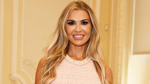 Christine McGuinness in a pink dress smiling at a camera.