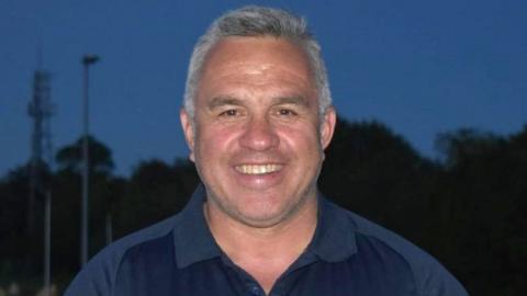 Sgt Matt Ratana smiling with short grey hair wearing a navy blue polo shirt.