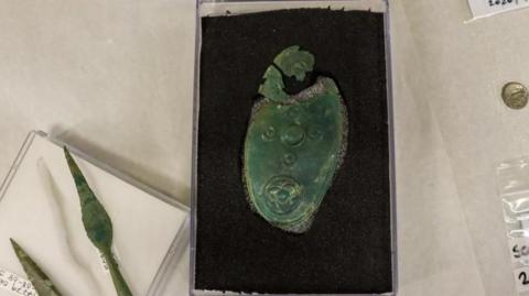 A close up of miniature iron and copper-alloy shields and spearheads on a table in cases