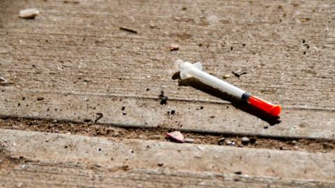 A used needle is discarded on the ground. 