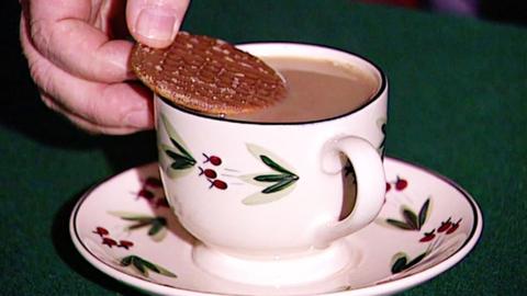 A chocolate digestive biscuit being placed on top of a cup of tea