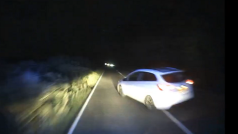 A blurry dashcam image from an ambulance shows a white car turning onto an A-road in front of the ambulance at night