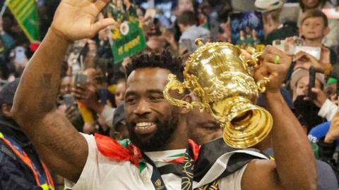 Captain Siya Kolisi greets supporters as he holds the Webb Ellis Cup upon the South African rugby team's arrival