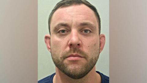 A police mugshot of Grant Eddleston, who has short brown hair and stubble, looking into the camera with a blank expression