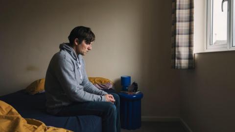 A man sitting alone in his bedroom