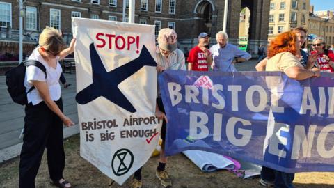 Protestors standing outside City Hall on the grass, holding up banners and signs which read "Bristol Airport is big enough". 