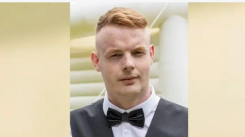 A head and shoulders shot of a young man wearing a black bowtie and waistcoat. He has ginger hair cut short.