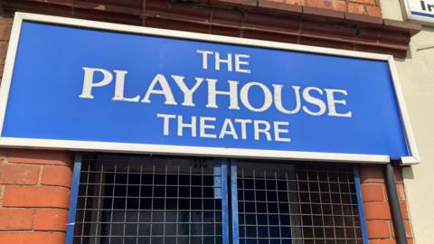 The front of the theatre with a blue sign emblazoned with The Playhouse Theatre in white writing and blue gates