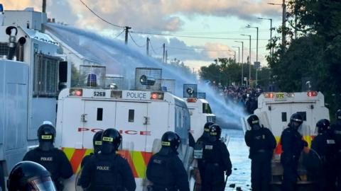 Water cannon fired from white police trucks at groups of people