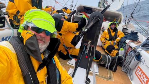 Bob is wearing waterproofs on a boat at sea. There are other crews in the background.