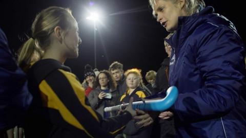 Leah Wilkinson hands over a hockey stick