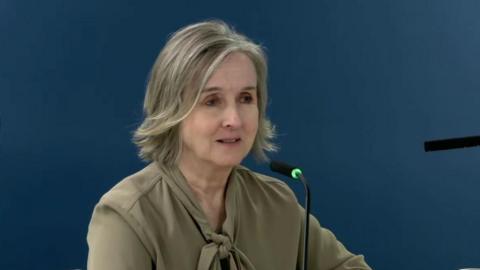 Briege Donaghy, chief executive of the RQIA, speaking at the UK Covid-19 inquiry. She has shoulder length dark grey hair and is wearing a khaki coloured blouse