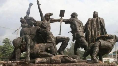 A bronze monument depicting miners in a dramatic struggle with armed colonial-era police. Several figures are shown resisting or collapsing, while one officer raises a weapon toward the workers. The sculpture captures the tension and violence of the historical confrontation at the Iva Valley coal mine.