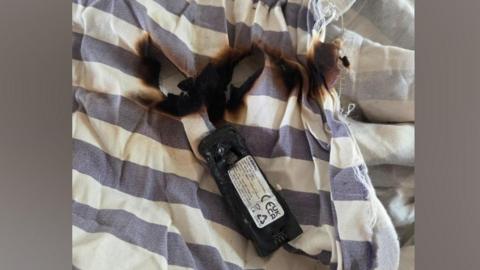 A damaged battery and burnt bedding. The bedding is blue and white stripes.