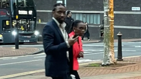 Tai Yasharahyalah, in a black suit, and Naiyahmi Yasharahyalah, in a red jacket, walking to court