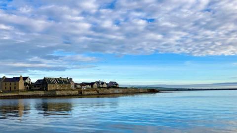 Houses on a peninsular sandwiched between blue water and blue sky with white clouds