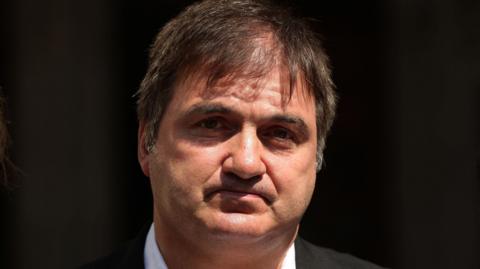 Barry George, dressed in a suit looks at the camera. He has black hair