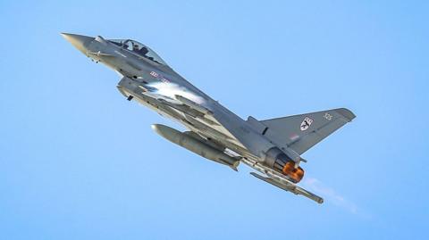 British Royal Air Force Eurofighter Typhoon jet flies upwards into a clear blue sky.