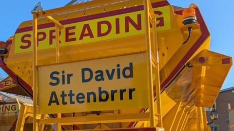 Yellow gritting vehicle with Sir David Attenbrrr on its rear.