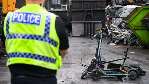 Dorset Police implement the crushing of illegal e-scooters and e-bikes at Silverlake Auto Salvage Centre in Southampton, on 2 July 2025 in Southampton, England. A police man watches on at a bunch of e-scooters.