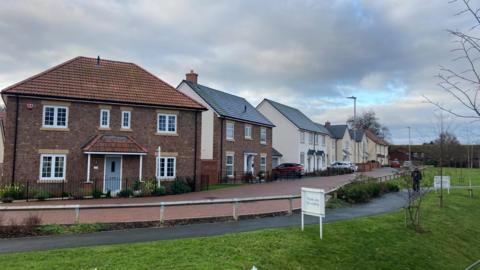 An existing row of houses on the Liddymore Park Development. The houses are a mix of red brick and white stones. There is a footpath running along the front.