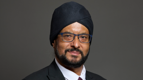A headshot of a man in a turban on a grey background.