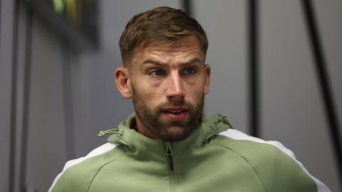 Charlie Taylor looks slightly to his left with a slightly stunned look on his face and mouth slightly open. he wears a green zip up jumper.