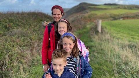 George with his two sisters and mother lined up behind him walking some cliffs. They are smiling. 