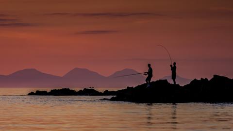 Men fishing with sunset over Jura behind them