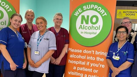 The University Hospital Liverpool Group’s Alcohol Care Team stand around a poster, smiling, which reads 'We support no alcohol in hospital'.