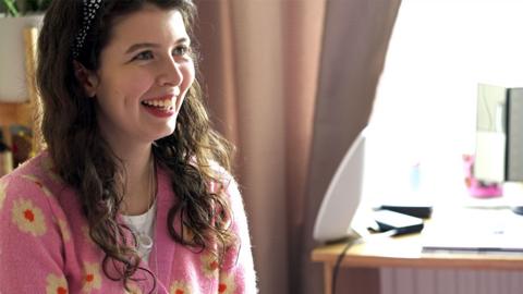 Elspeth in her apartment, sitting on a bed and laughing