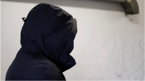 A trafficking victim with their hood up to hide their identity is speaking to a reporter in a car park 