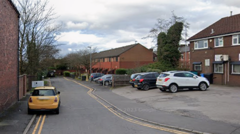 A yellow mini, parked on double yellow lines, at the entrance to Plumpton Close with houses on the right