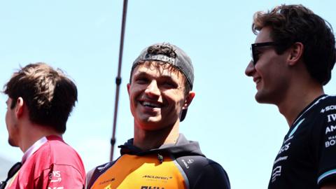McLaren's Lando Norris smiling with George Russell to the right and Charles Leclerc to the left
