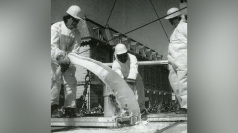 Three men pour batter through tubes. The picture is black and white.
