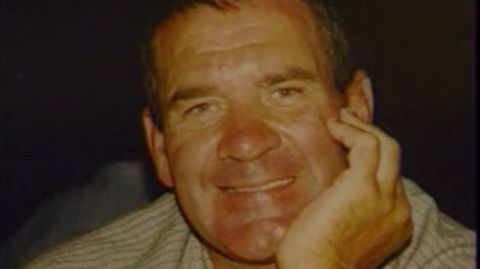 Michael Steele smiling and leaning on his hand. He is wearing a white shirt with fine black stripes.