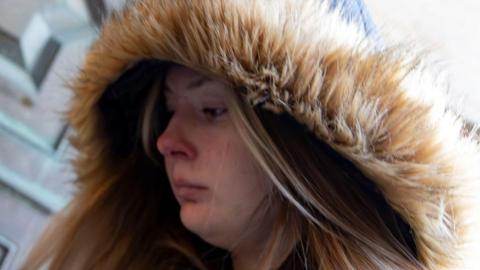 A young woman with a fur-lined hood enters a court building