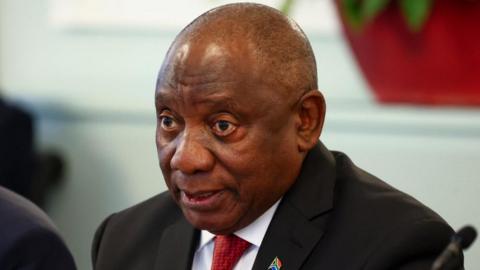 A head-and-shoulders shot of Cyril Ramaphosa. He is wearing a dark jacket and red tie.