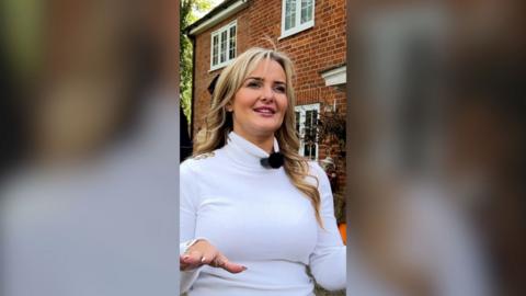 Lauren Marshall stands in front of a house in Yateley. She has blonde hair and a white top.