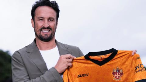 Cesar Peixoto holding a Wolves shirt while smiling